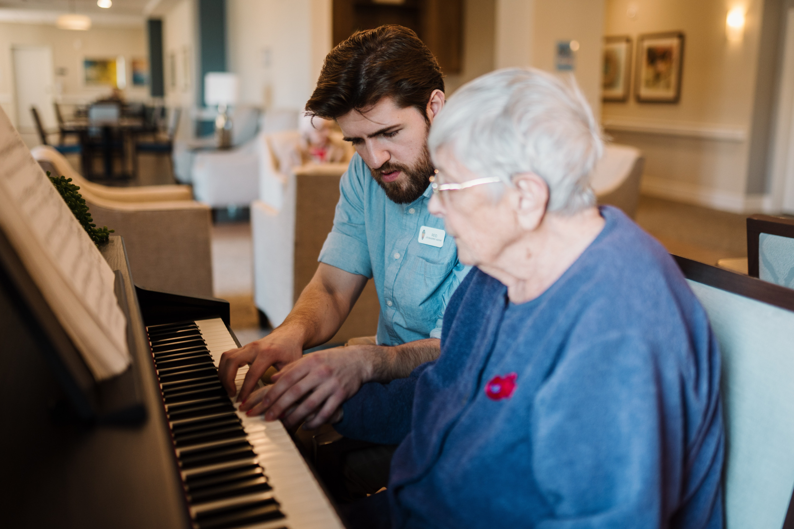 A staff member helps a resident play the piano.