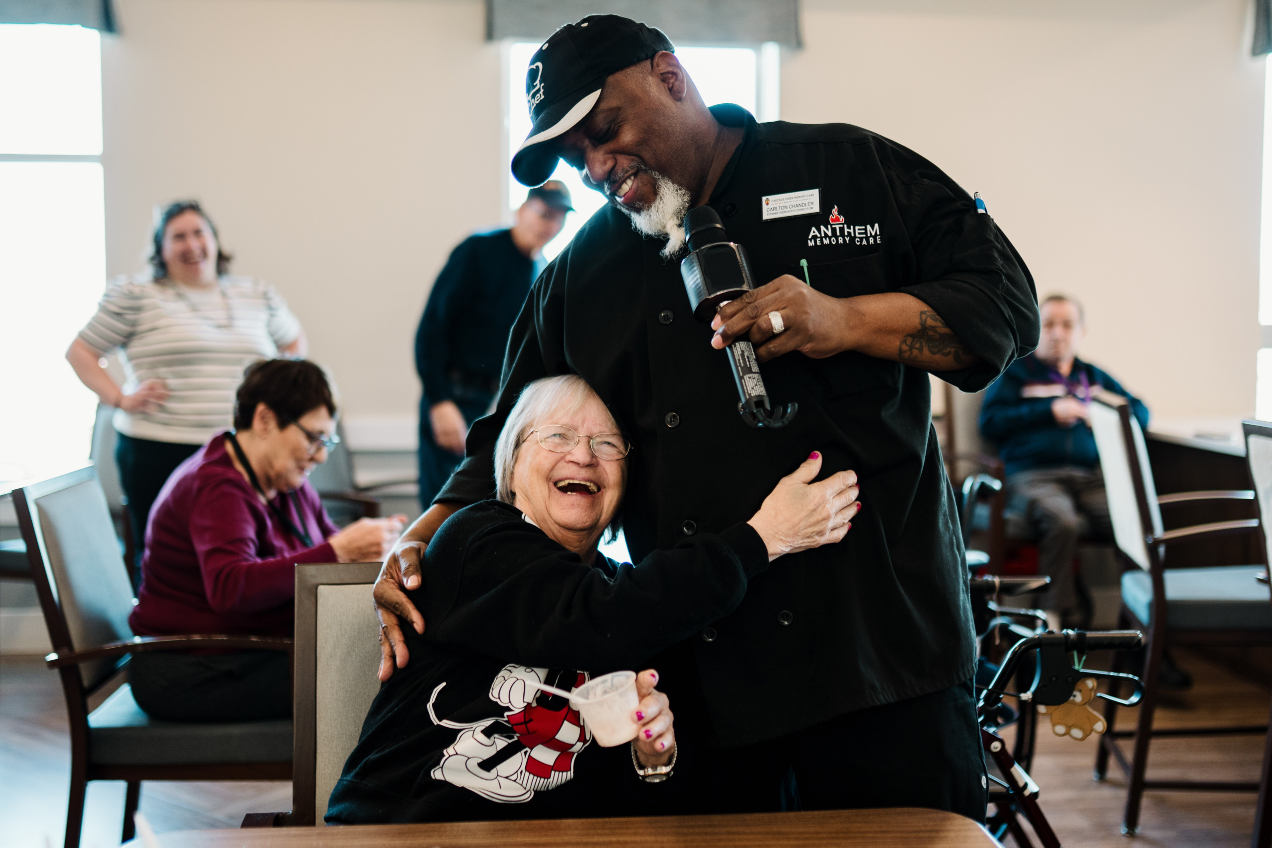 Our dining services manager sings karaoke while getting a hug from a smiling resident